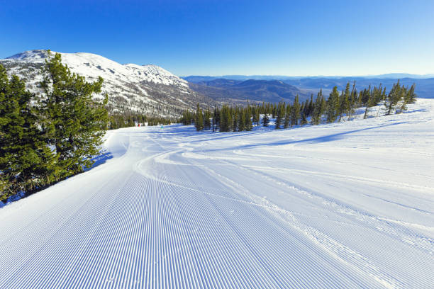 velluto di neve e cielo blu sulla pista da sci sul monte green, stazione sciistica di sheregesh. pista da sci e snowboard preparata con traccia di battipista sulla neve. bella giornata invernale soleggiata per lo sport, il tempo libero - ski trace foto e immagini stock