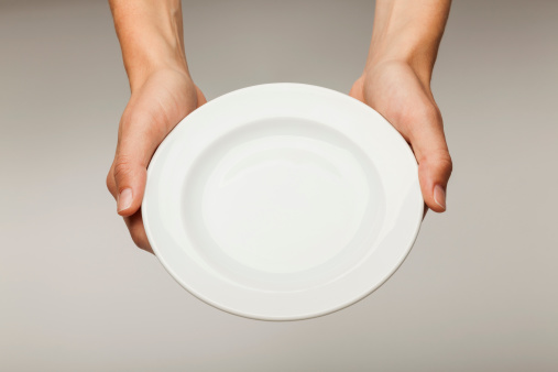 A pair of female Caucasian hands holding a blank white plate against an off white beige background.  Entire photo is in focus. 
