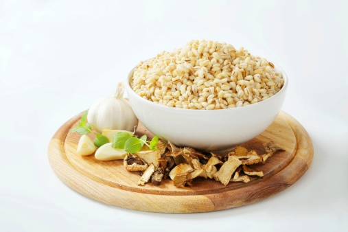 pile of cooked peeled barley in a white ceramic bowl with vegetable garnish on a round wooden cutting board