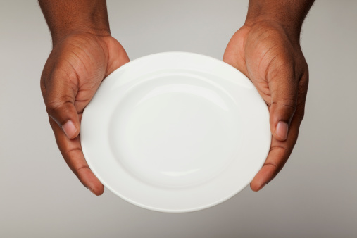 A pair of male African American hands holding a blank white plate against an off white beige background.  Entire photo is in focus.