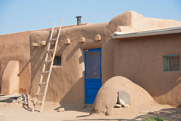 Ladder on Adobe Pueblo with Kiva Oven "A simple wooden ladder leans against an old adobe pueblo building that is outfitted with a brightly painted door and windows, and a kiva oven for outdoor cooking in the summer." stove oven adobe outdoors stock pictures, royalty-free photos & images