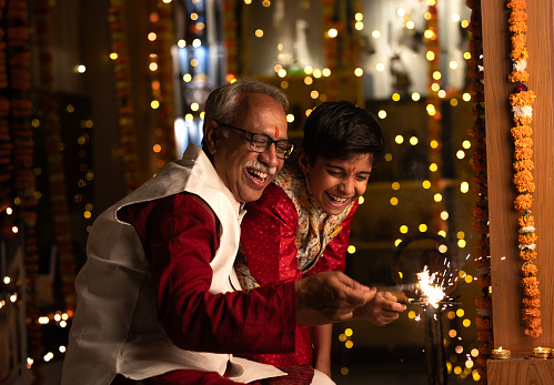 Grandfather and grandson playing with sparkler while sitting at home during Diwali festival