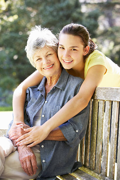 Grandmother With Teenage Granddaughter Sitting On Bench Together Grandmother With Teenage Granddaughter Sitting On Bench Together Smiling To Camera senior adult women park bench 70s stock pictures, royalty-free photos & images