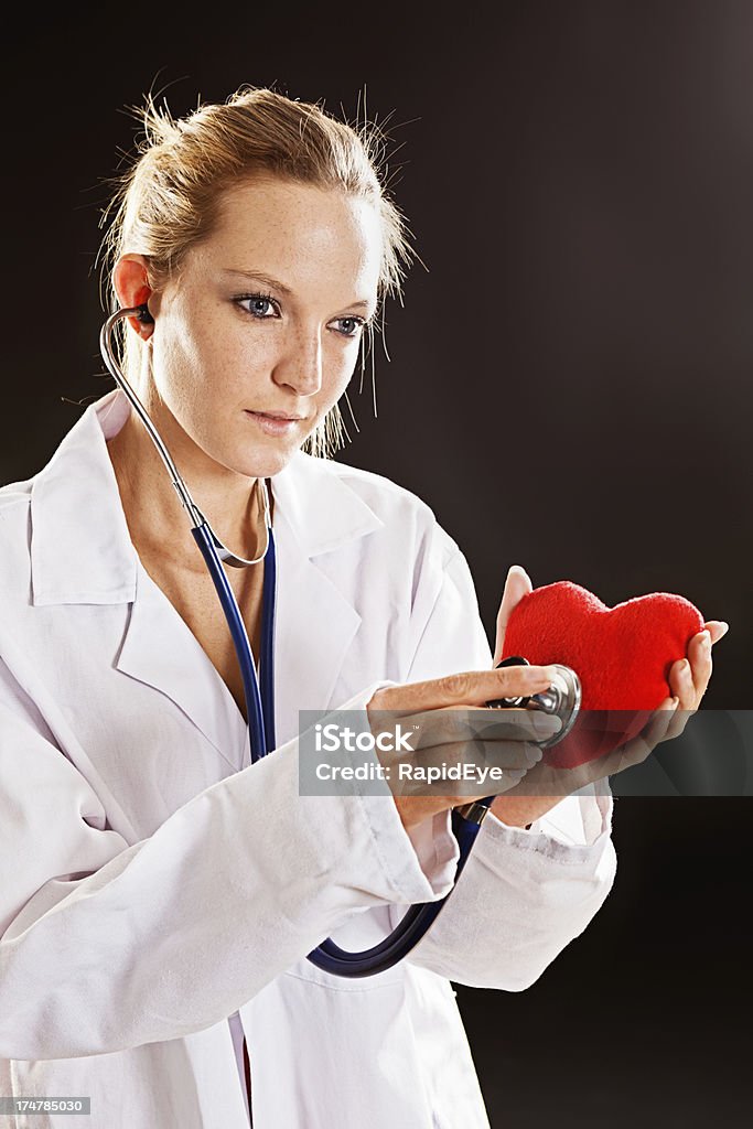 Серьезные молодая женщина врач проверяет День святого Валентина сердце с Стетоскоп - Стоковые фото Женщины роялти-фри