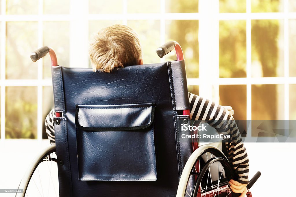 Ragazzino ruote la sua sedia a rotelle verso il soleggiato finestra - Foto stock royalty-free di 8-9 anni