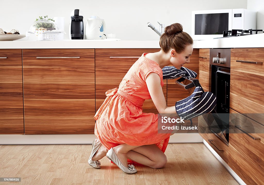 Man preparing dinner A woman wearing oven mittens checking out her dinner in the oven. Cooking Stock Photo