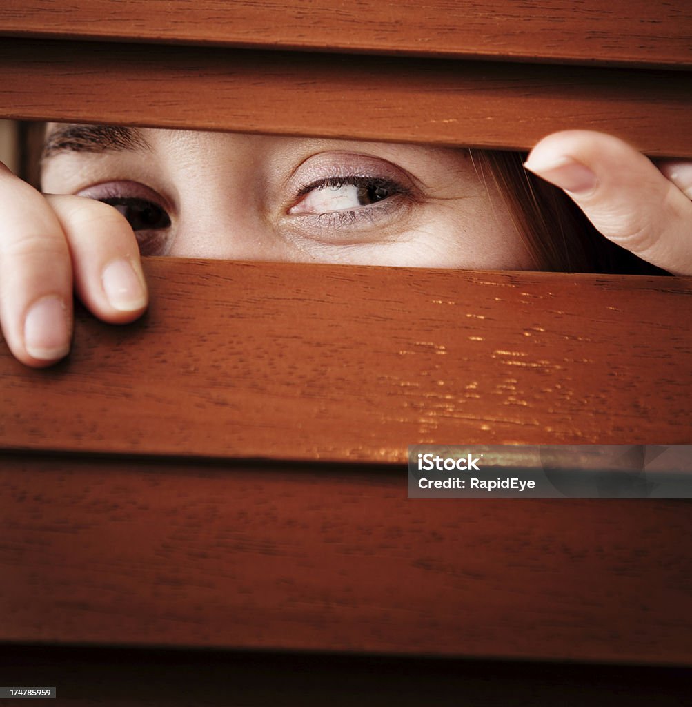 Jeune femme remarquer à travers des stores vénitiens en bois, souriant - Photo de Curiosité libre de droits