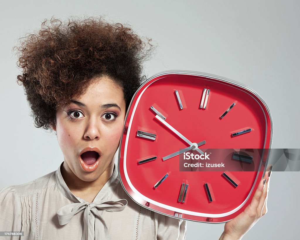 Afro Girl with Clock Portrait of teenaged afro girl holding a big red clock next to her head, staring at the camera. Studio shot, grey background. 18-19 Years Stock Photo