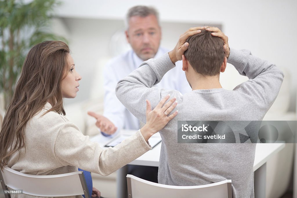 Couple with consultant. Young couple having conversation with consultant. Man holding his head in hands.See more LIFESTYLE and MEDICAL images with this COUPLE and DOCTOR or CONSULTANT. Click on image below for lightbox. 50-59 Years Stock Photo