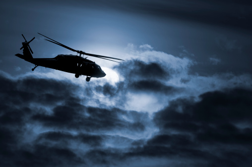 The silhouette of an army helicopter flies across a dramatic moonlit night.Get the separate elements in the image here: