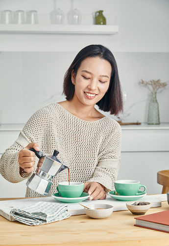 Portrait of a beautiful and happy asian girl in the kitchen, early bird morning routine, drinking coffee, representing positive attitude and a healthy lifestyle, an image with a large copy space