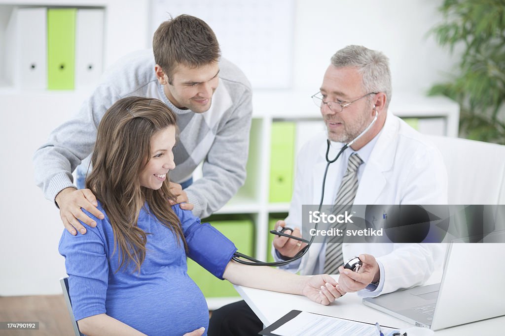 Pregnant woman with husband at doctor's office. Pregnant woman with husband at doctor's office measuring blood pressure.See more LIFESTYLE and MEDICAL images with this COUPLE and DOCTOR or CONSULTANT. Click on image below for lightbox. 50-59 Years Stock Photo