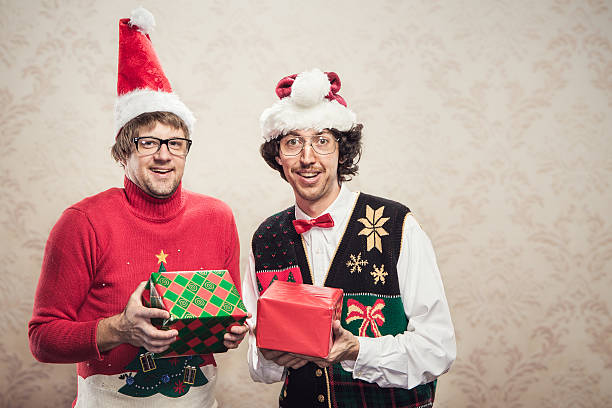 Christmas Sweater Nerds Two goofy looking men in ugly looking Christmas cardigans and sweaters (complete with matching red bow tie and a classy mustache).  One man opens a gift that his friend has given him.  Damask style vintage wall paper in the background.  Horizontal with copy space. nerd sweater stock pictures, royalty-free photos & images
