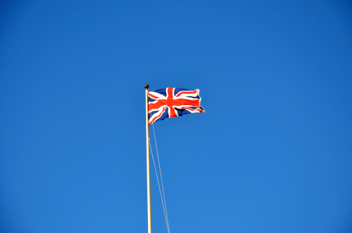 A large Union Flag (erroneously known as the Union Jack) flying aloft a flagpole with a clear blue sky behind. Good copyspace and room for crops on any side.