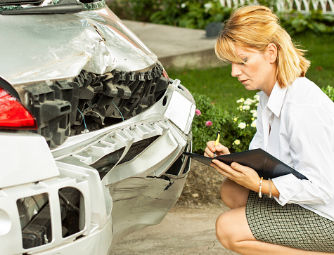 An insurance adjuster looking at the damaged bumper of a car