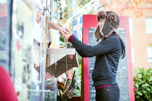 A beautiful young woman looks at a menu at a food cart pod in Portland, Oregon, trying to decide what to order.  Horizontal with copy space.