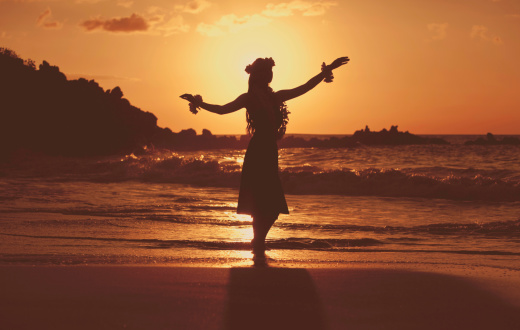 Young Hula Dancer posing for the camera seaside at sunset time backlit.