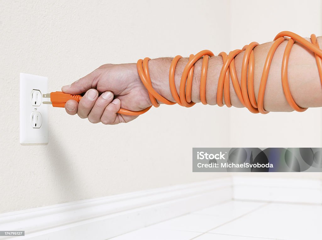 Energy Constricting A electrical cord squeezing around an arm plugging in the plug. Squeezing Stock Photo