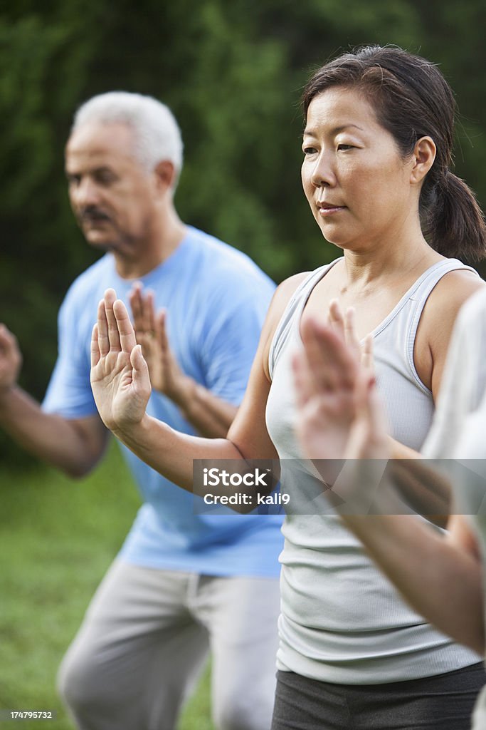 Tai chi class Multi-ethnic group of adults practicing tai chi in park.  Focus on Asian woman (40s). Tai Chi Stock Photo