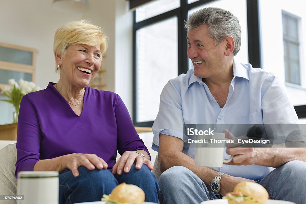 Sênior casal sorri e compartilha de café da manhã em um apartamento - Foto de stock de 65-69 anos royalty-free