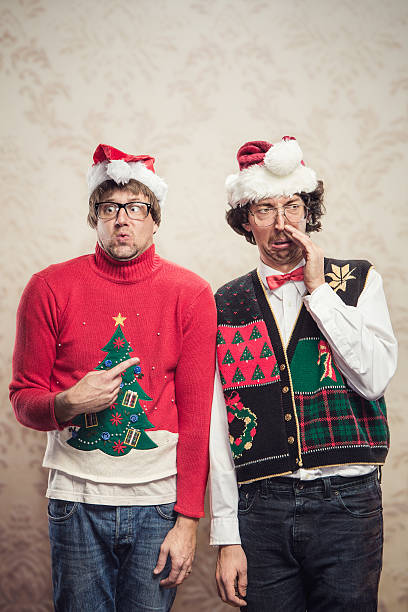 Christmas Sweater Nerds Two goofy looking men in ugly looking Christmas cardigans and sweaters (complete with matching red bow tie and a classy mustache) stand looking awkward for a holiday photo.  Damask style vintage wall paper in the background.  Vertical with copy space. christmas ugliness sweater nerd stock pictures, royalty-free photos & images