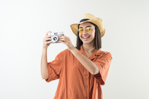 Happy young girl with old camera, hat and sunglasses in studio. Tourist in ochre or orange shirt on sightseeing trip.