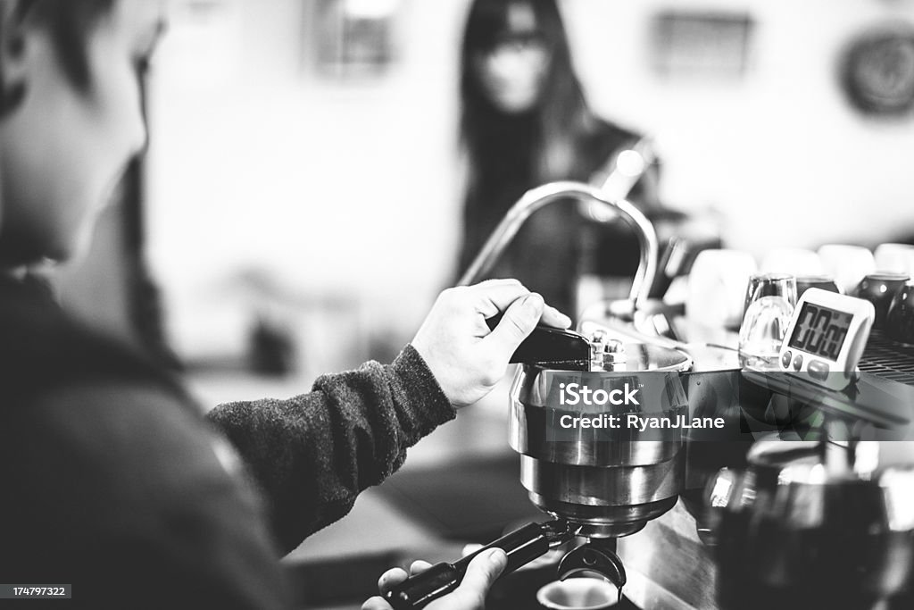 Coffee Shop Latte A coffee shop barista prepares an espresso latte while a customer waits in the background at a cafe.  Horizontal; SHALLOW DEPTH OF FIELD.  Black and white image. Adult Stock Photo