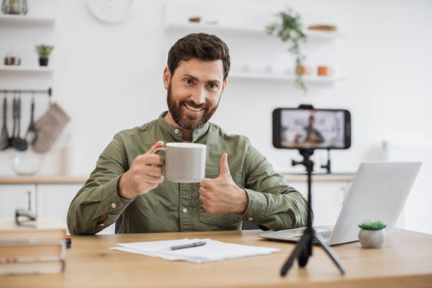 istock Brunette man recording vlog and holding cup in hand indoor 1747984251