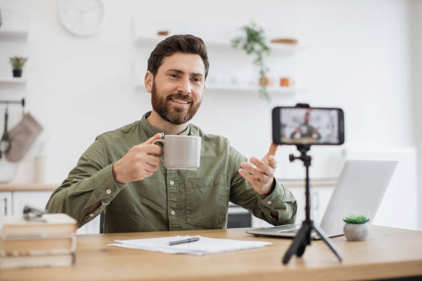 istock Brunette man recording vlog and holding cup in hand indoor 1747984262