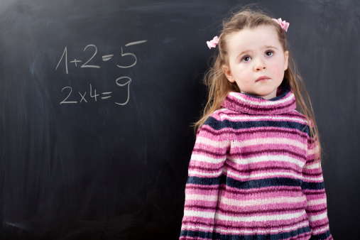 A cute girl in front of a black chalkboard. There is a math calculation on the board. The result is wrong.