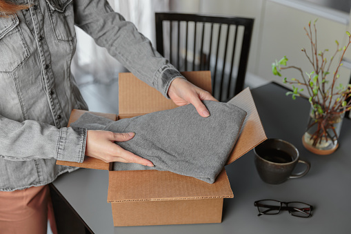 Second hand clothes in cardboard box. Woman packing box with used wardrobe for resale. Circular fashion, fast fashion, Sustainable ethical consumption and shopping, thrifting shop concept.