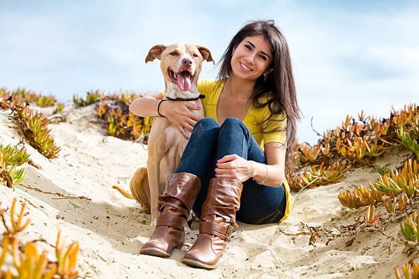 Young woman with her dog on a sandy beach.