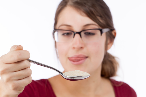 A young woman looks at a spoon full of suger with a tempting look in her eye.