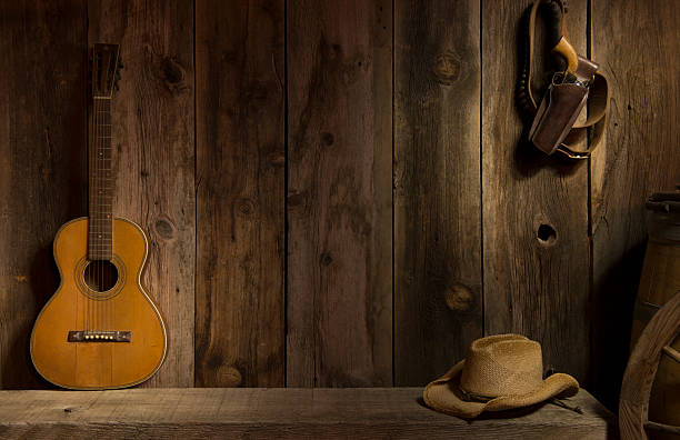 Wild West scene "An outdoor Western scene with copy space. Included are the essentials of the Old West with a six shooter and gun belt, straw hat and the old vintage parlor guitar on a bench next to the side of a barn." wagon wheel bench stock pictures, royalty-free photos & images