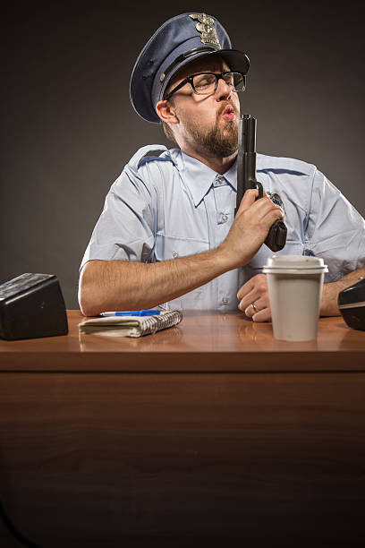 oficial de policía soplando la parte superior de la pistola en satisfacción - desk police police station humor fotografías e imágenes de stock