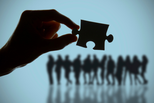 Hand holding jigsaw puzzle piece over group of people