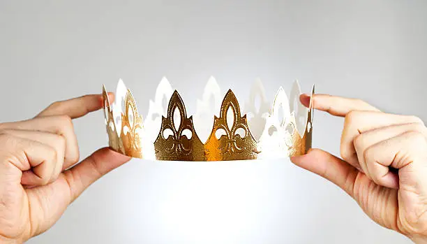 Hands holding a golden paper crown.
