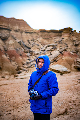 Young boy in hoodie is posing with his camera in the desert of Bárdenas Reales, Navarra, Spain.