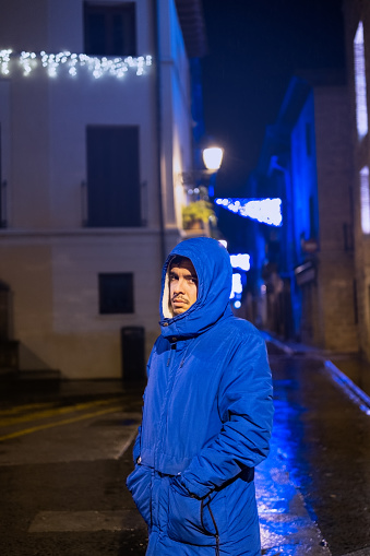 short medium shot portrait of a young hooded boy posing in the rain in a rural village of Spain.