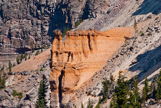 Pumice Castle Rock Formation An eruption occurred 70,000 years ago and formed the pink, buff and orange Pumice Castle formation on what is now the east side of Crater Lake. Subsequently it was buried by the Redcloud Cliff flow and then exposed when Mount Mazama erupted and its caldera collapsed. Rain and wind have since finished the job of carving the pumice into its hoodoo shaped formations. Pumice Castle sits about 1,300 feet above the surface of Crater Lake in Crater Lake National Park, Oregon, USA. jeff goulden crater lake national park stock pictures, royalty-free photos & images