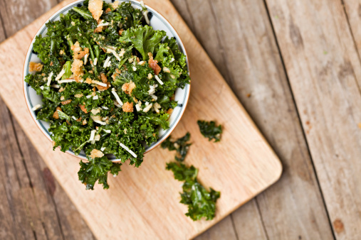 An overhead close up shot of a white bowl full of healthy kale salad. Shot on a grungy old wooden background.