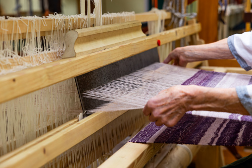 Woman is warping a wooden handloom. Hands holding a heddle hook and threading the table loom. Weaving tools