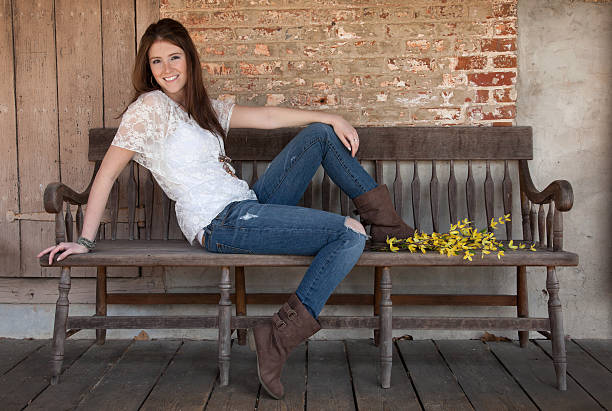 A country beauty smiles for the camera while seated on an old fashioned bench.