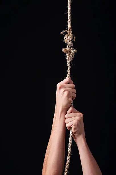 Photo of Two hands clinging hopelessly to a rope about to break