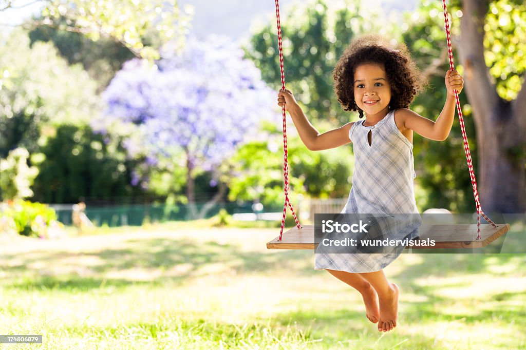 Sorridente giovane ragazza su un Altalena nel parco - Foto stock royalty-free di Bambino