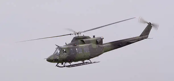 a Huey helicopter in flight against an overcast sky
