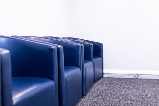 Waiting room from a clinic with four blue chairs with a white wall in the background