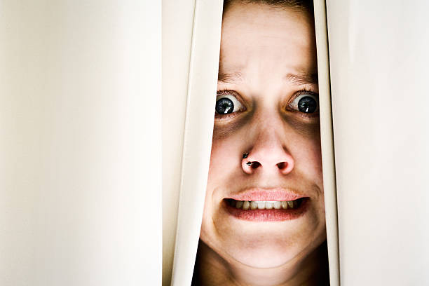 istock Terrified young brunette woman peeps through drapes, grimacing 174808348