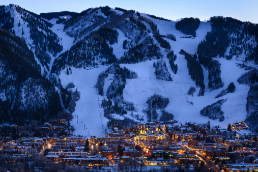 Dusk image of glowing lights in town and cut ski runs and slopes above.  Scenic view with copy space.  Captured as a 14-bit Raw file. Edited in 16-bit ProPhoto RGB color space.