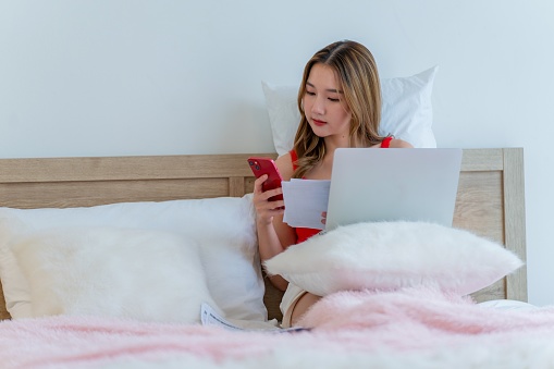 A Generation Z female takes control of her financial destiny from the cozy comfort of her bed. Embracing the convenience of online finance management, she leverages digital banking and financial tools to secure her financial independence, anytime and anywhere.